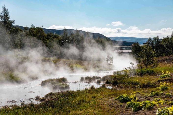 Scenic photo of hot spring water flowing through beautiful green landscape, giving a misty look