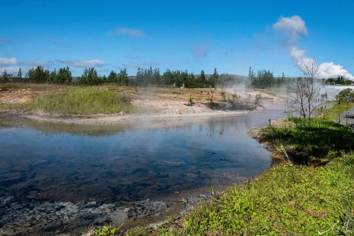 Scenic photo of hot spring water flowing through beautiful green landscape, giving a misty look