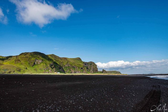 Beautiful photo of the black sandy beach with fresh green mountain and bright blue sky