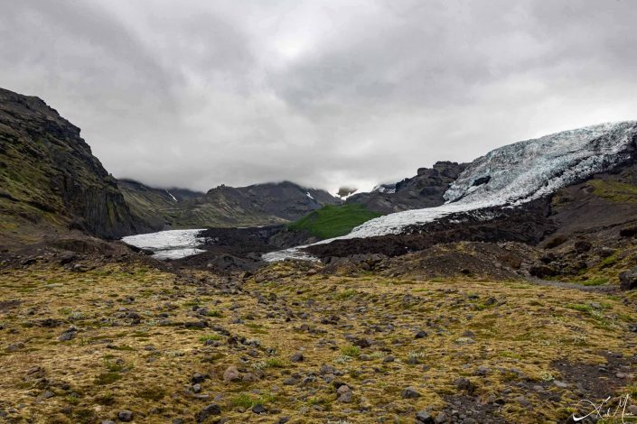 Scenic photo of Icelandic glacier with mountains in the background and yellow-green foreground