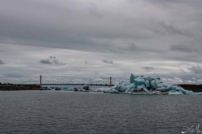 Best close-up photo of a iceberg, with blue and black layers and a bridge in the background