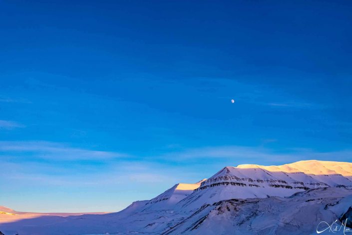 Scenic photo of snow covered mountains with clear blue sky and moon