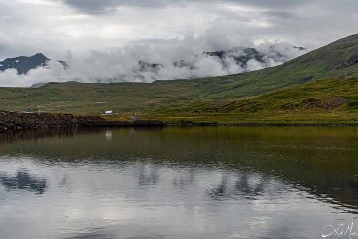 Scenic photo with green brown mountain in the background with clouds descending on its top and its reflection in the water
