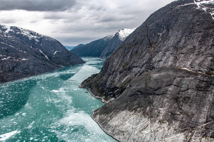 Scenic photo of brown/ grey mountains with green/emerald coloured water in between in the valley