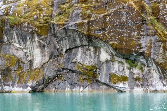 Green-grey rock along with a blue- turquoise water in the front