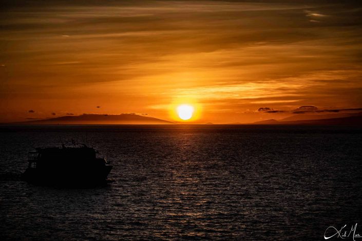 Beautiful sunset photo with shades of orange by the sun and its glow in the dark waters along with a little boat passing by