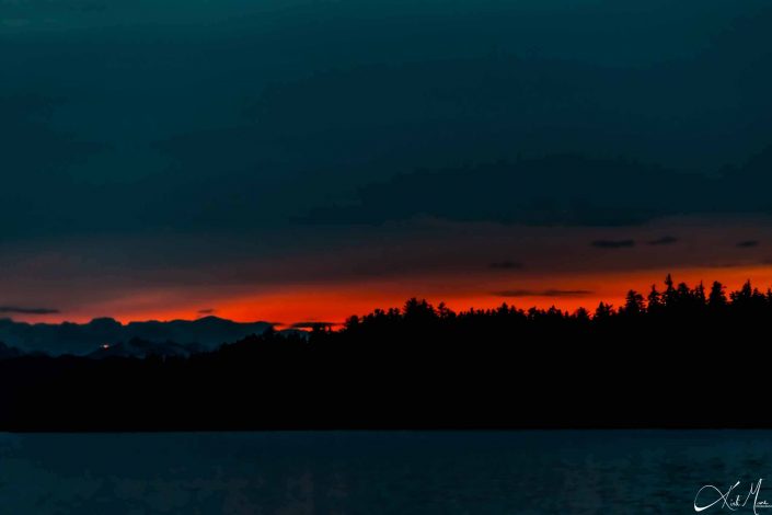 Beautiful sunset with dark shades of blue and pink-orange with snow-capped mountains and trees