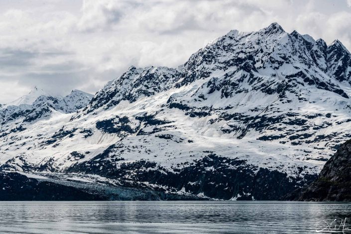 Snow covered mountain along with a glacier meeting the silvery-grey waters