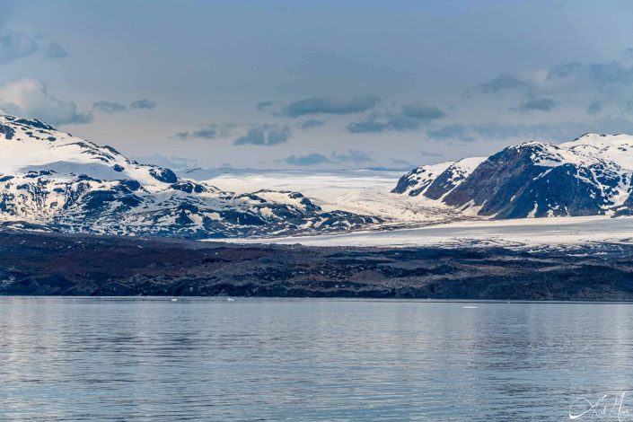 Snow covered mountain along with a glacier meeting the silvery-great waters