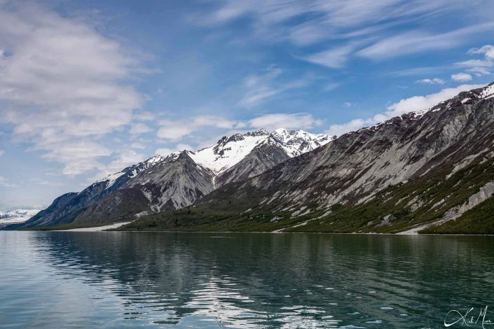 Snow capped grey-green mountains with dark grey-silvery waters in the front