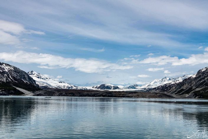 A glacier along with snow capped grey-green mountains with blue-silvery waters in the front