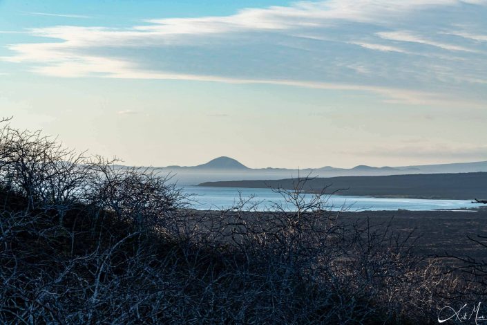 Scenic photo of a volcanic terrain with sky blue waters in the middle and mountains in the background