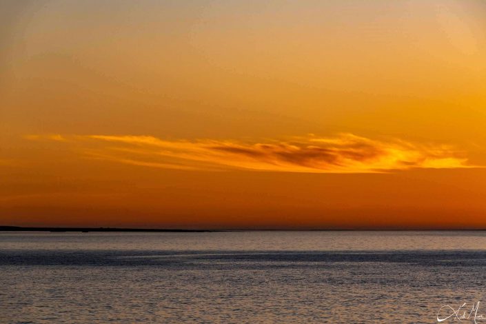 Beautiful scenic sunset with shades of orange in the sky with a dreamy cloud and silvery blue sea waters beneath