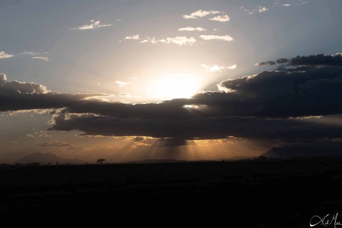 Great scenic photo of a cloudy sky in the middle and sun above while the sun rays filtering through the clouds and showing the beautiful silhouette of the landscape