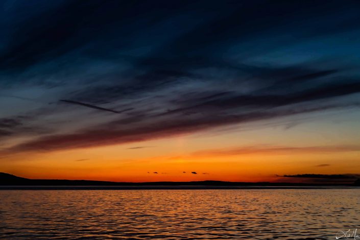 Best sunset photo with orange golden hues, deep shades of blue in the sky, silver blue waters and silhouette of the mountains in the background