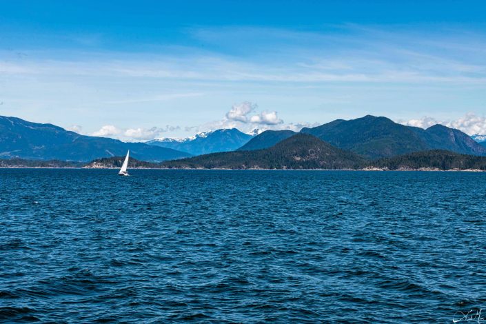 Beautiful photo of a boat sailing in blue waters and brilliant blue sky above, with mountains in the background