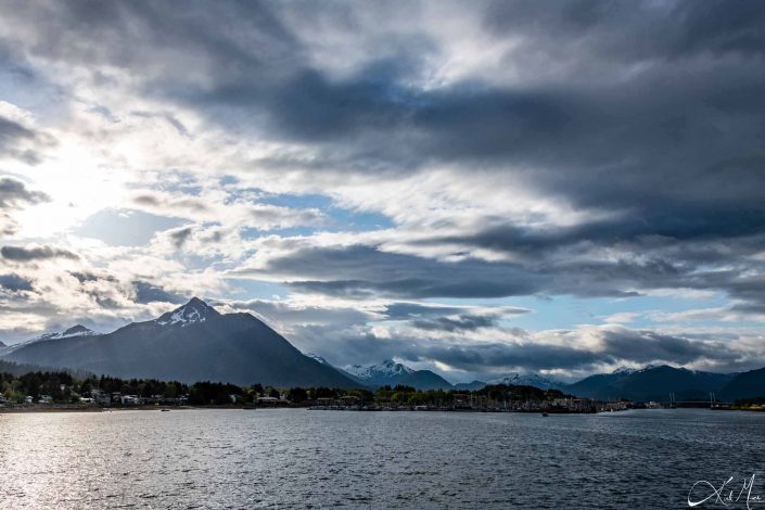 Scenic photo of snow capped mountains with stormy sky with clouds and silvery-grey waters in the front